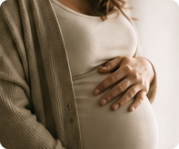 Pregnant woman in a soft cardigan resting her hands on her belly.